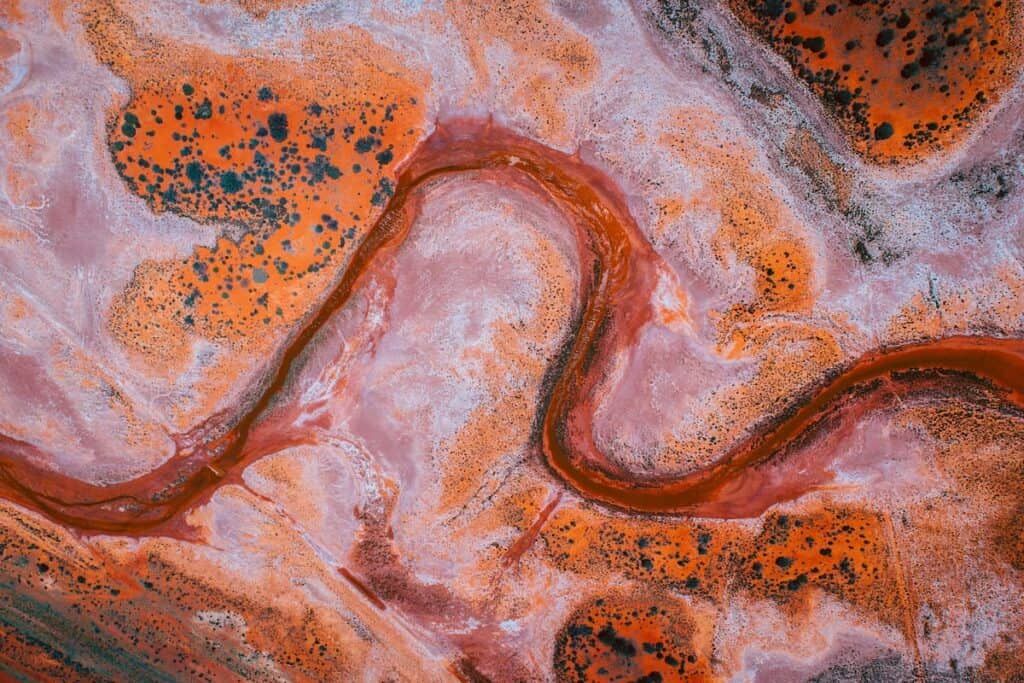 The patterns of Lake Ballard intensify with swirling textures of pink and orange, the natural mineral deposits creating abstract art from an aerial perspective.