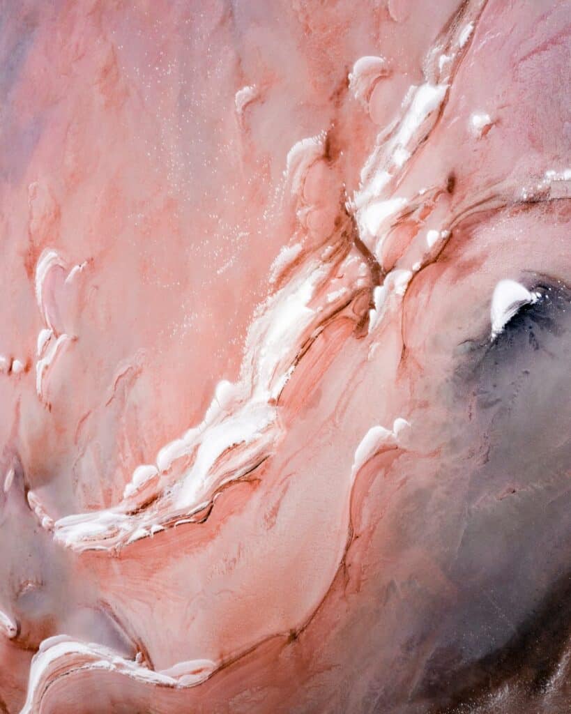 An aerial view of the Pink Lake near Cranbrook, displaying a mesmerizing mix of pink shades and white salt formations, with textures that resemble an abstract painting.