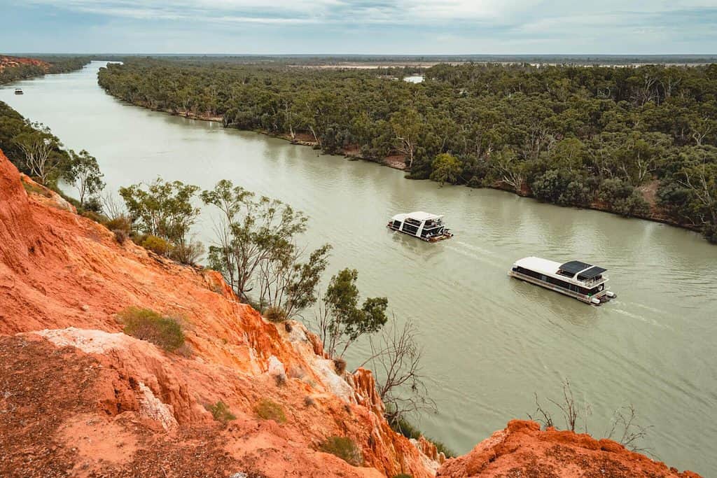 Green river with houseboats between red cliffs & green bushland